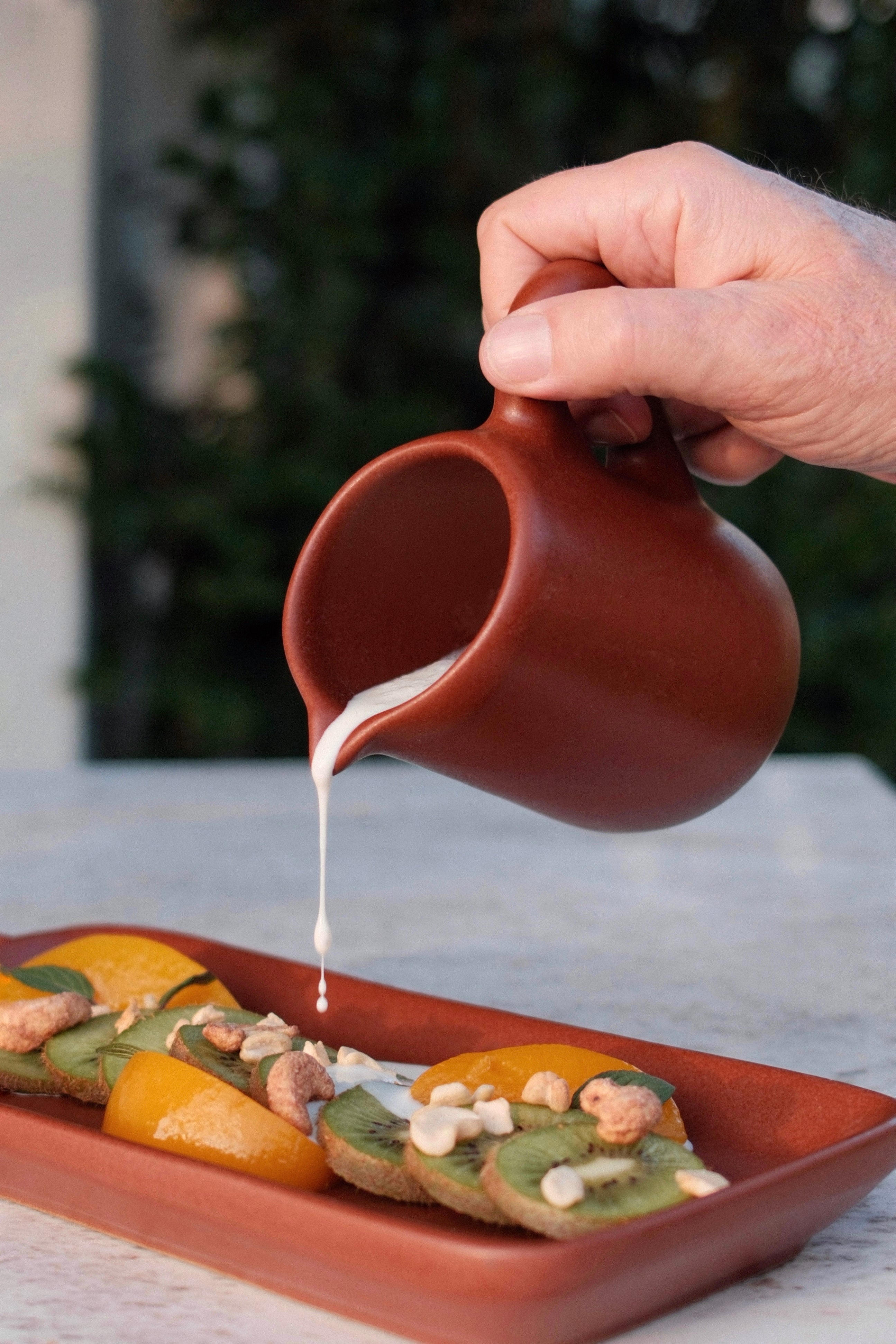 Small single-serve stoneware pitcher with narrow handle beside espresso cup