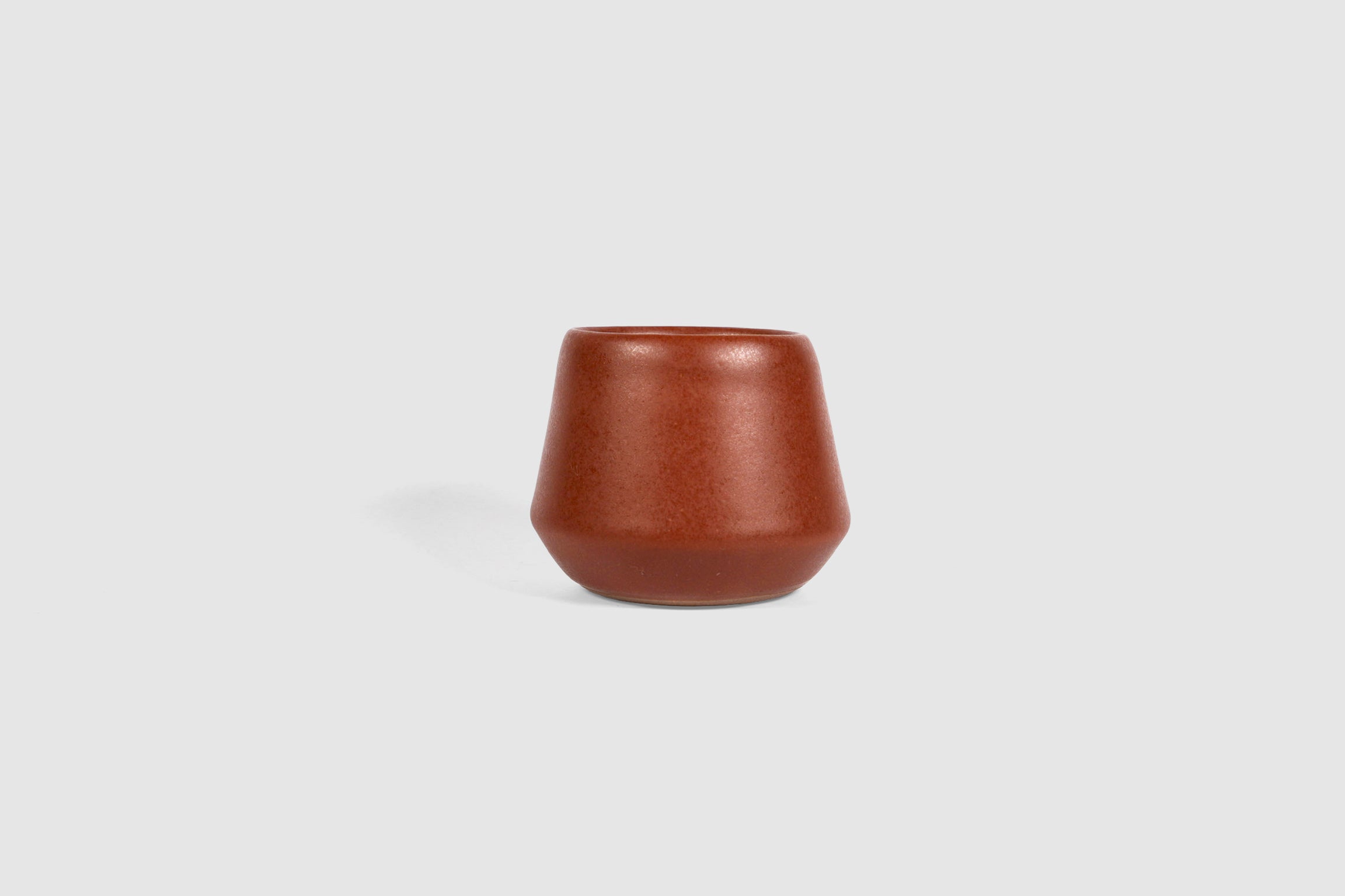 Small ceramic shot vessel with shouldered silhouette.