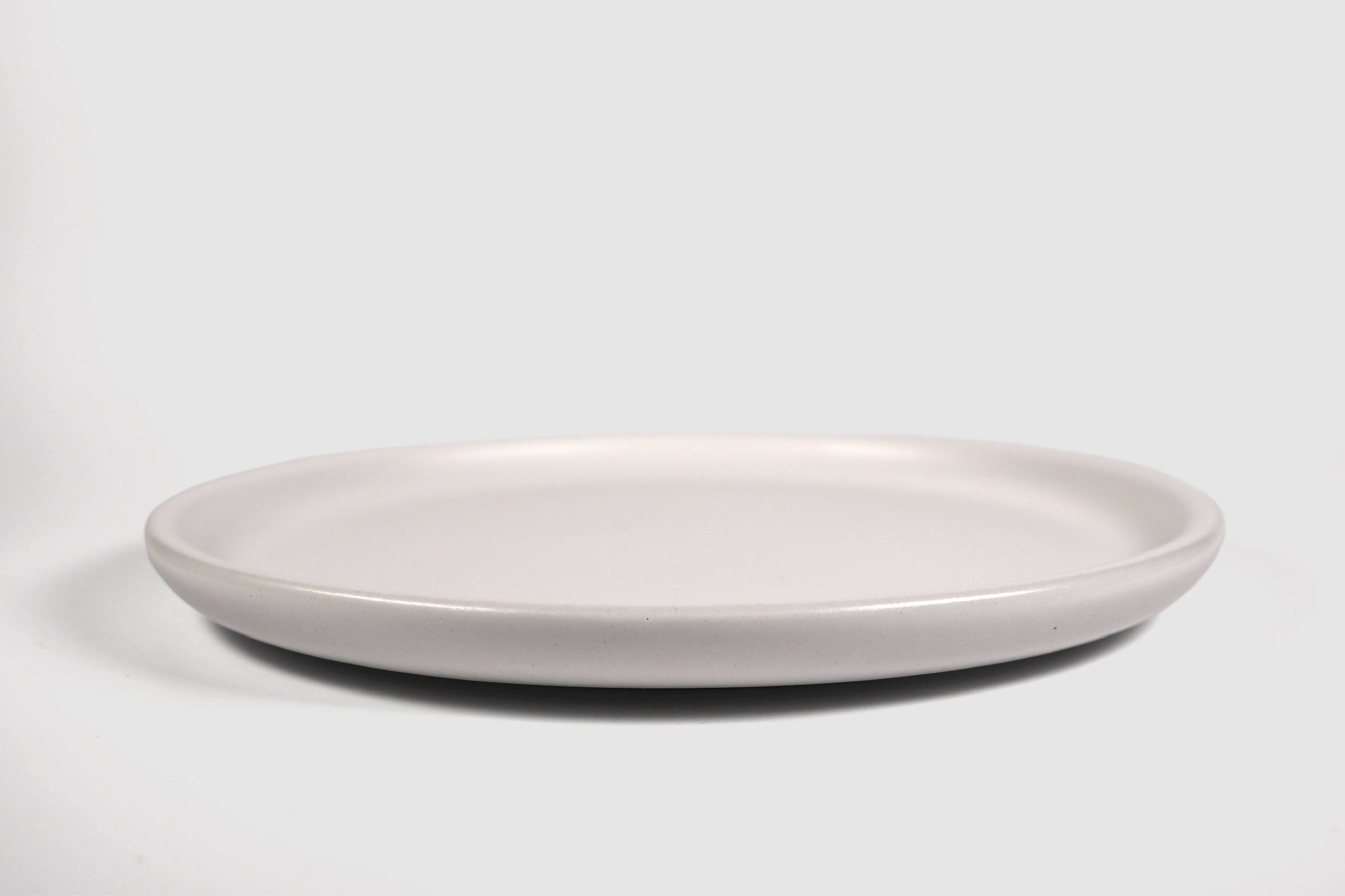 Stacked matte capuchino side plates with low lipped rim on pale ground