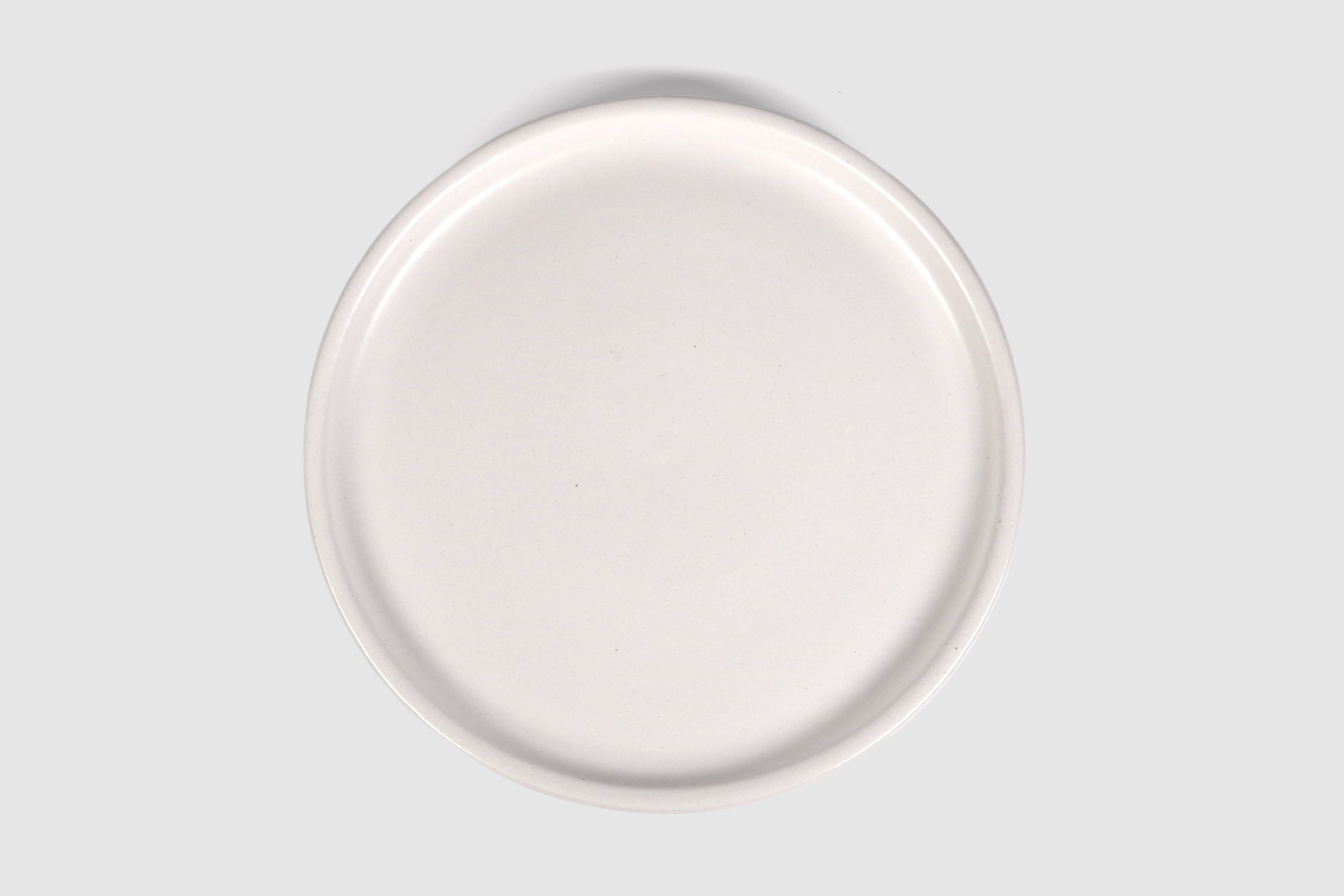 Stacked matte capuchino side plates with low lipped rim on pale ground