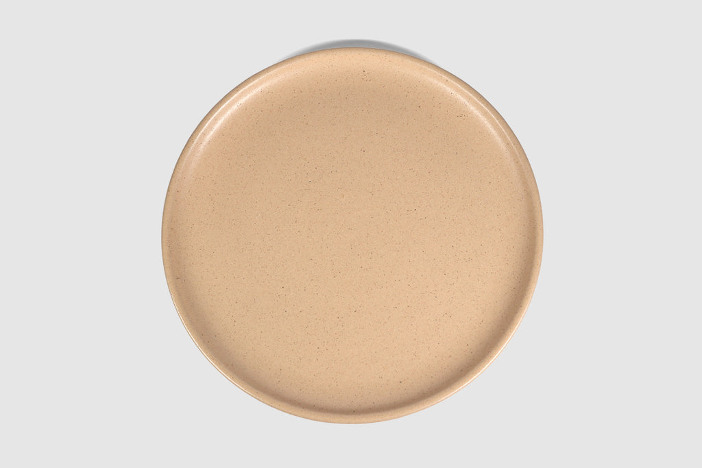 Stacked matte capuchino side plates with low lipped rim on pale ground