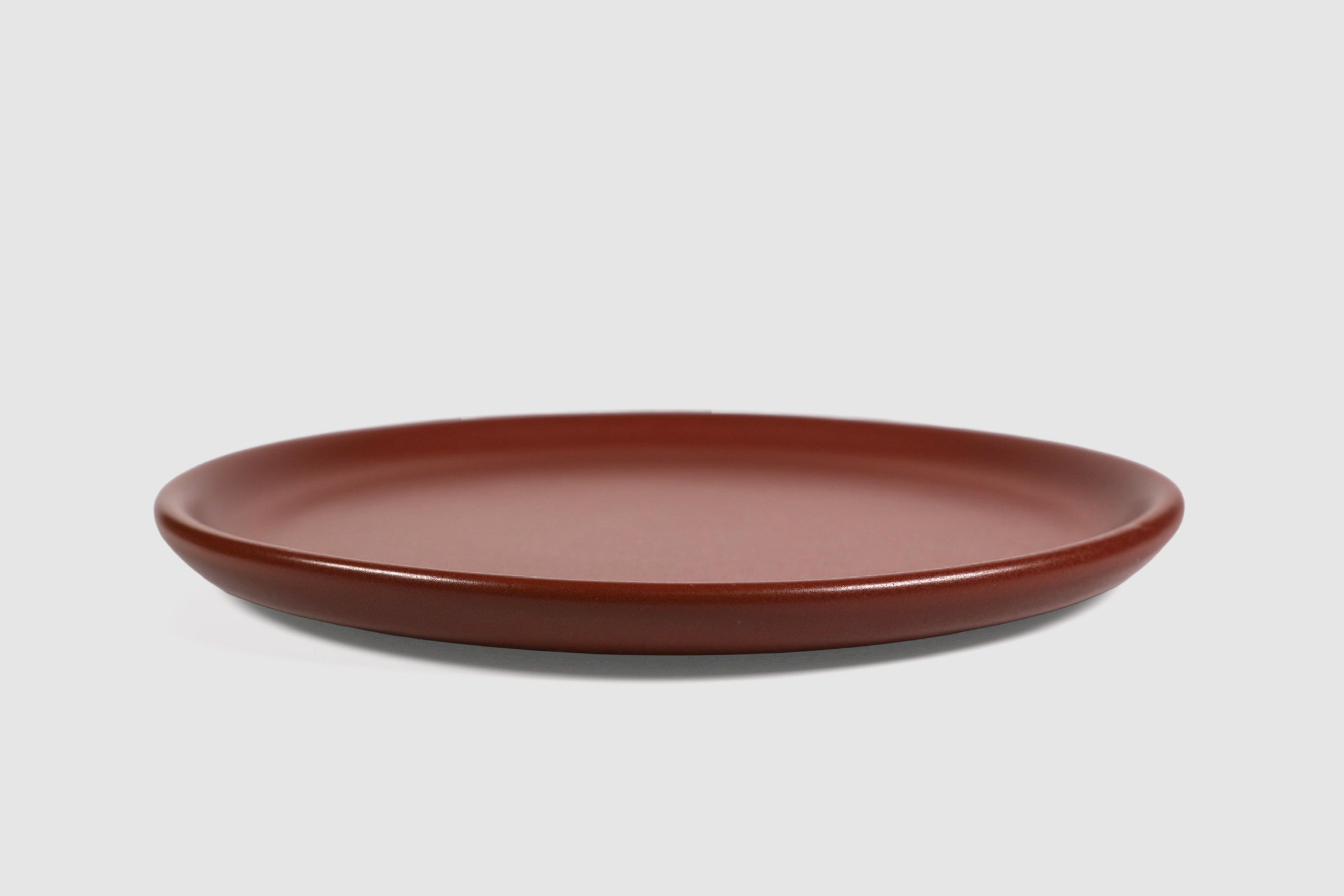 Stacked matte capuchino side plates with low lipped rim on pale ground