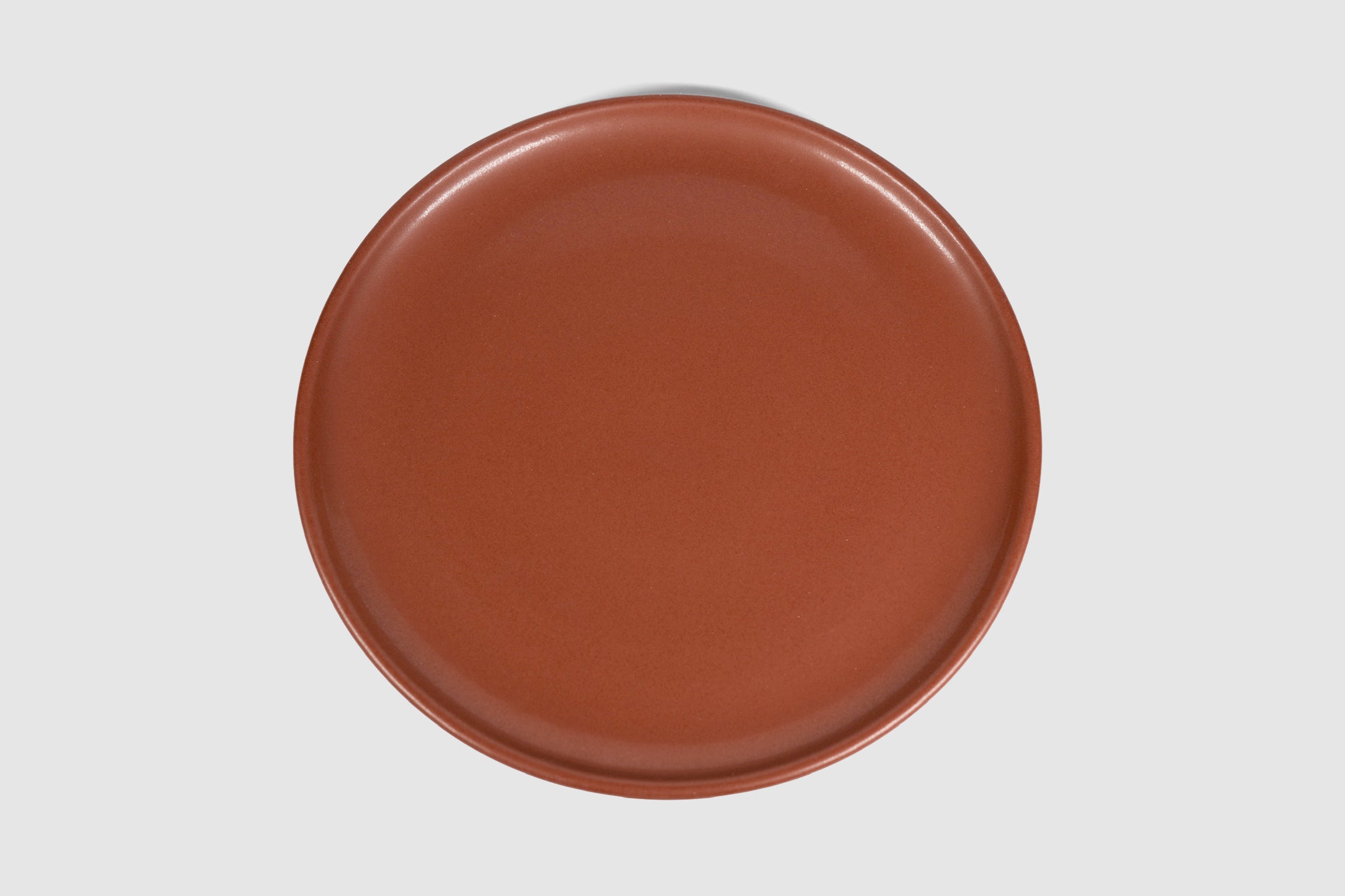 Stacked matte capuchino side plates with low lipped rim on pale ground