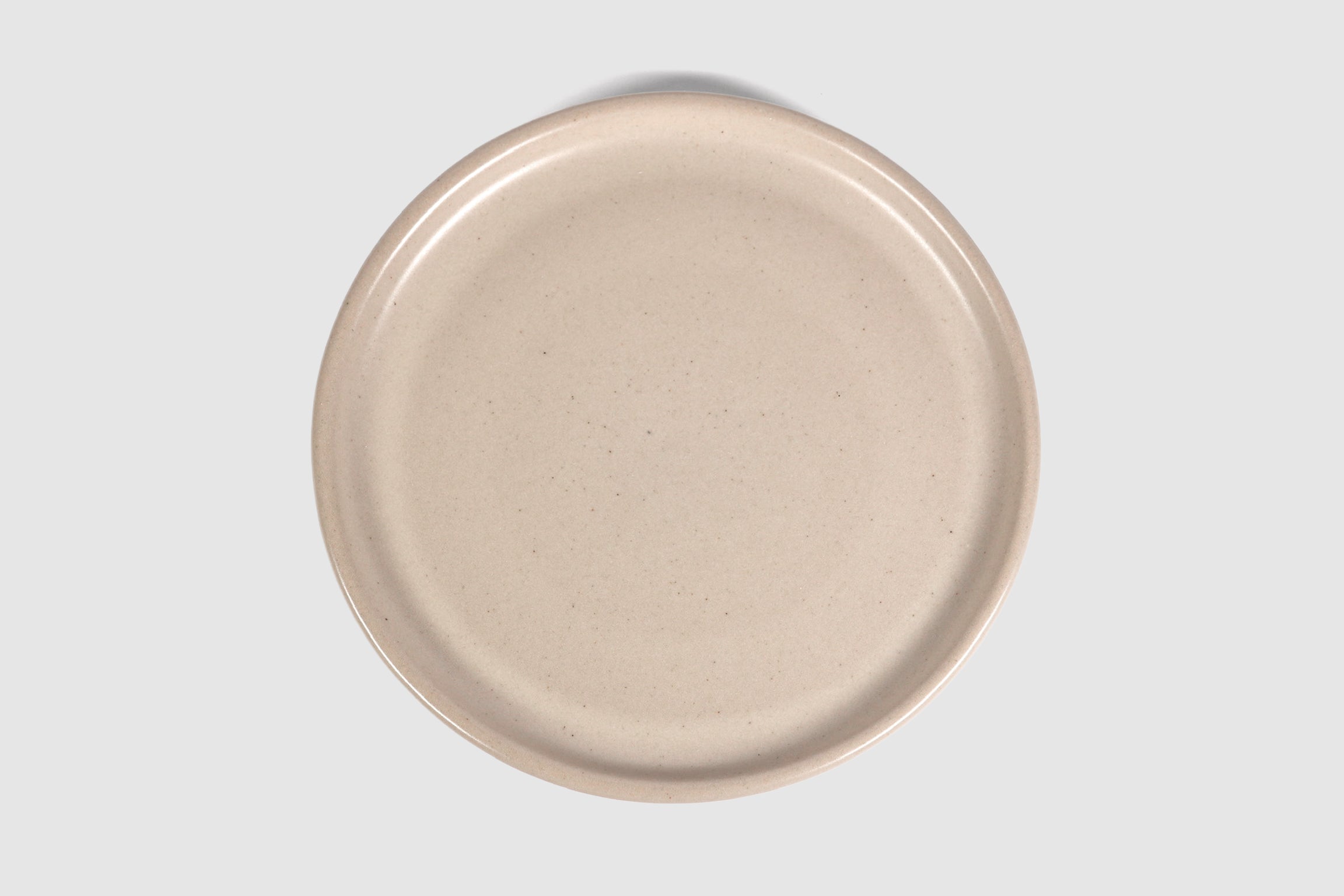 Stacked matte capuchino side plates with low lipped rim on pale ground