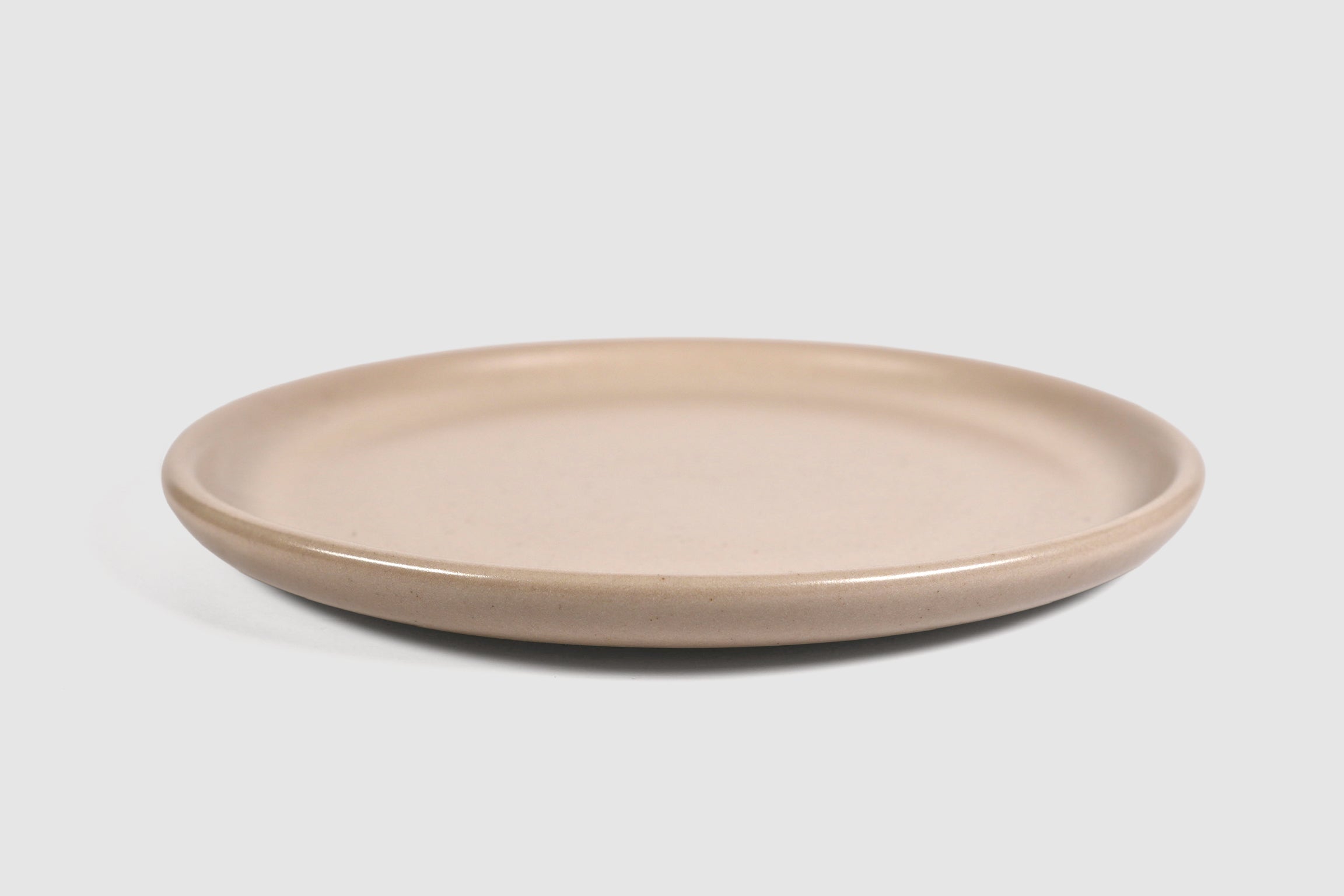 Stacked matte capuchino side plates with low lipped rim on pale ground