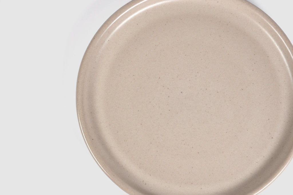 Stacked matte capuchino side plates with low lipped rim on pale ground