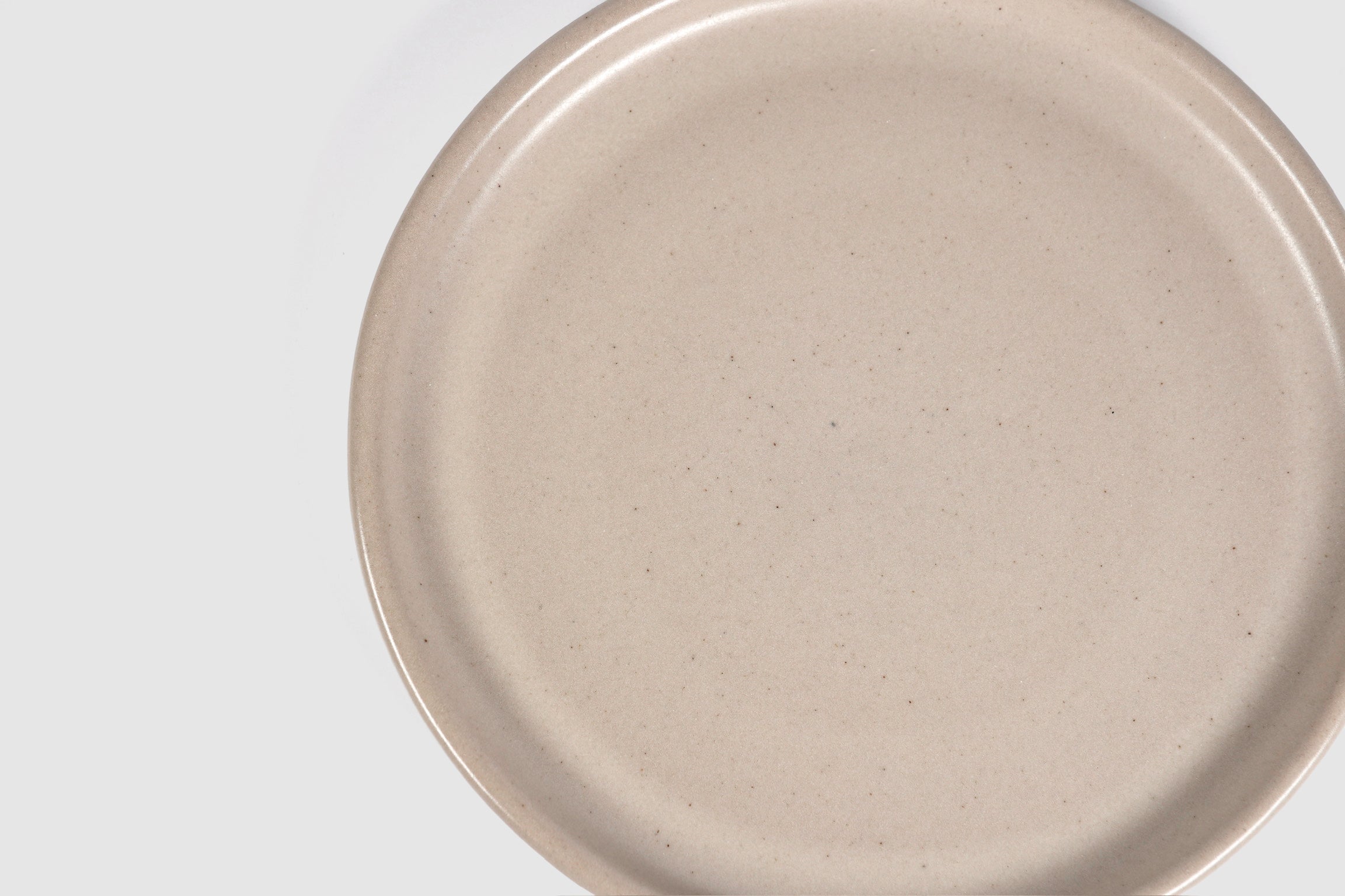 Stacked matte capuchino side plates with low lipped rim on pale ground